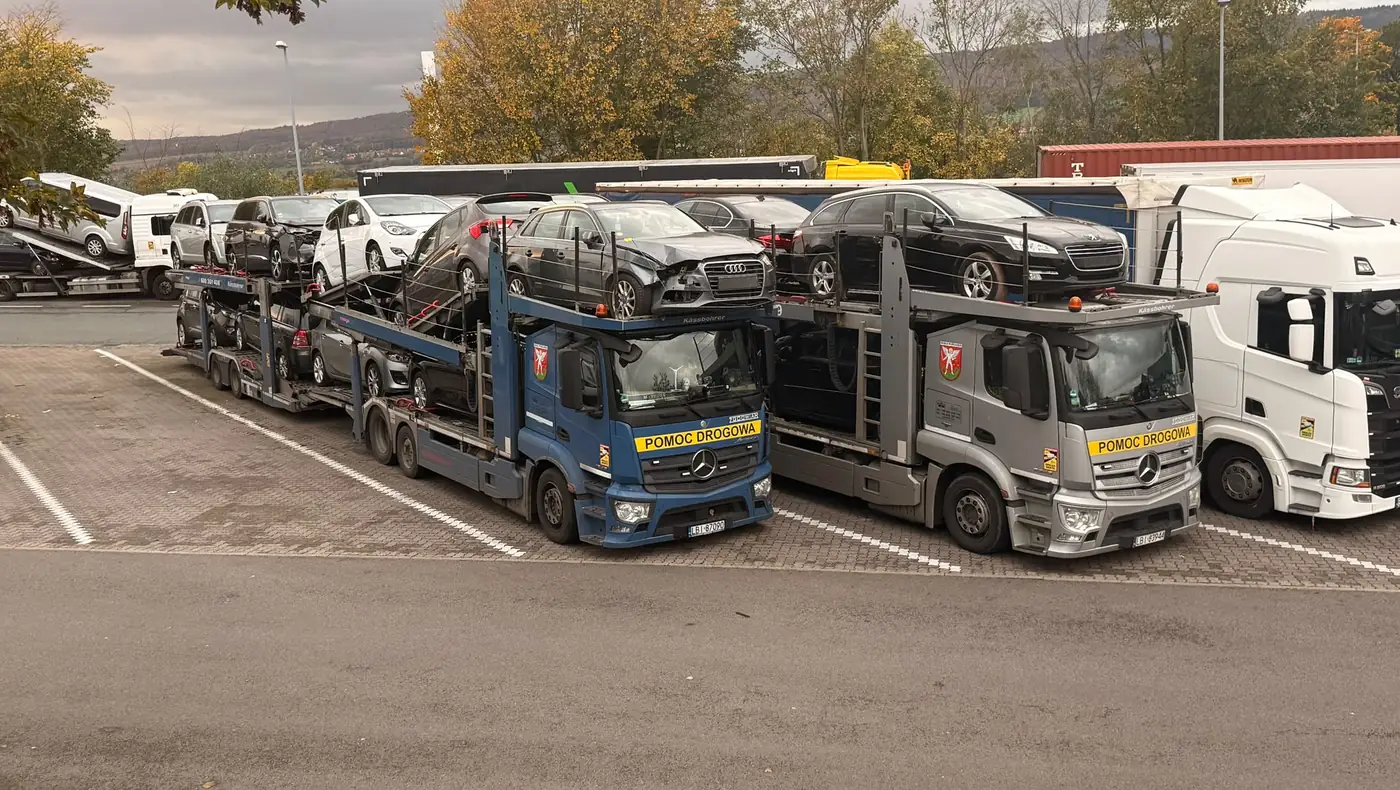 Dwa transportery ZGODWIAR załadowane samochodami, zaparkowane obok siebie.
