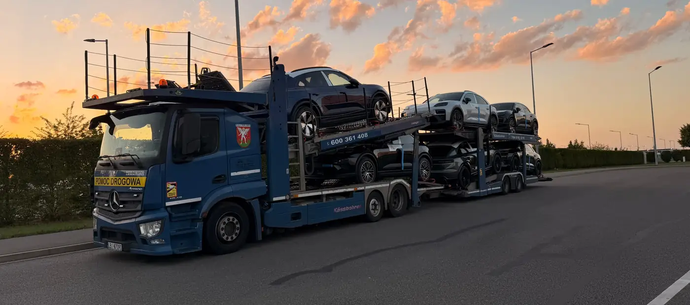 Transporter ZGODWIAR z załadowanymi samochodami na drodze, o wschodzie słońca.